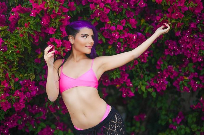 Retrato atmosférico de una modelo femenina posando al aire libre frente a un arbusto de flores rosas