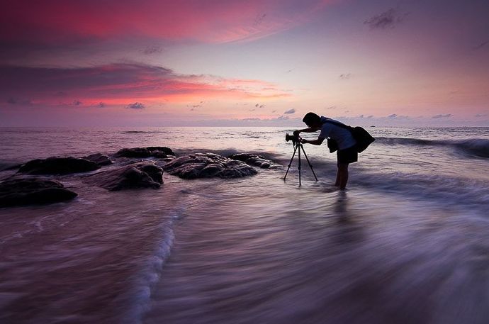 Un fotógrafo tomando fotos dramáticas del cielo en una playa con poca luz