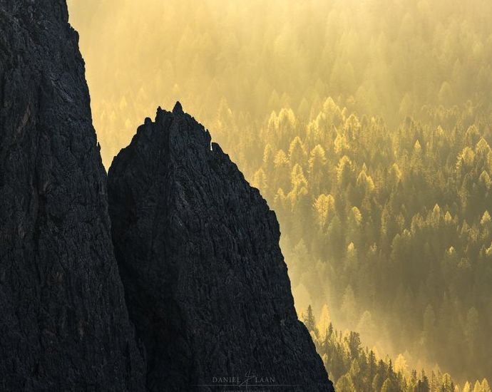 Una fotografía de paisaje artístico que muestra una montaña rocosa frente a un bosque verde y amarillo brillante.