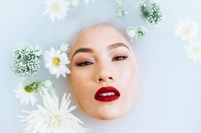 El rostro de una mujer emergiendo del agua rodeado por una flor, fotografiado con luz frontal