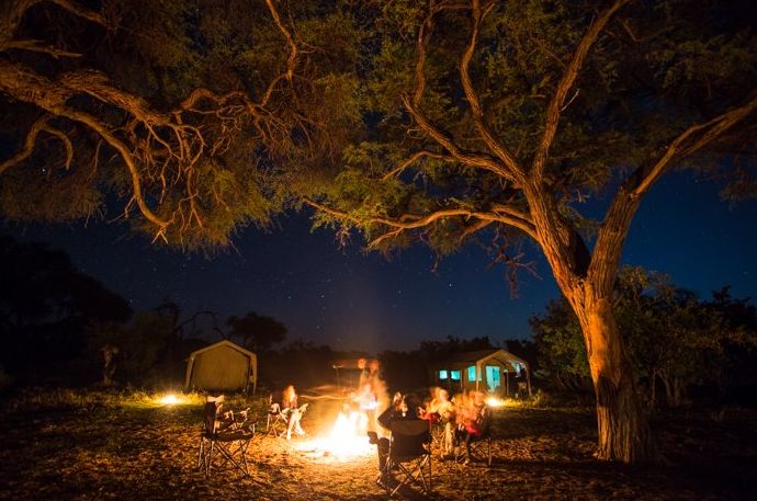 Personas sentadas alrededor de una fogata por la noche durante un viaje fotográfico de safari