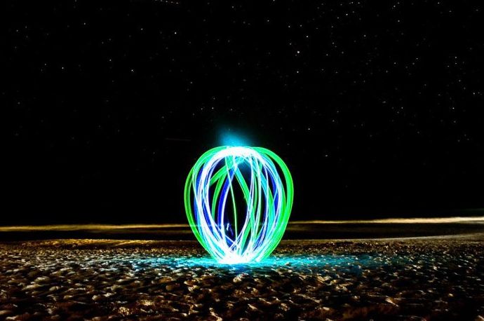 Una esfera de pintura de luz verde y azul en una playa por la noche.