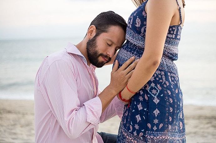 Linda sesión de fotos de embarazo de un padre sosteniendo el vientre de su esposa en la playa