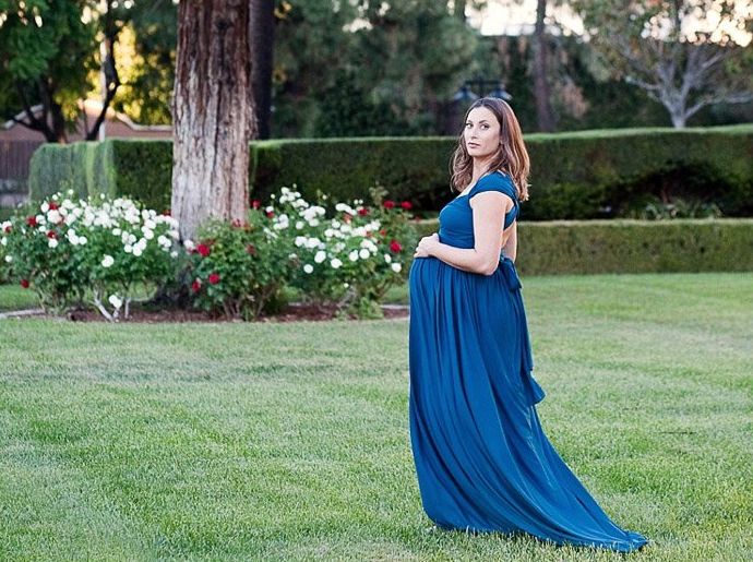 Una mujer con un vestido de noche azul posa al aire libre para una fotografía de maternidad
