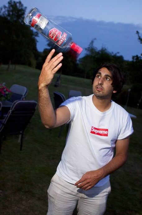 Un hombre haciendo malabares con una botella de vodka afuera con poca luz - fotografía de fiesta