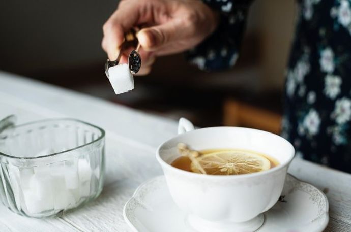 Detalle de ensayo fotográfico de alguien colocando un terrón de azúcar en una taza de té.