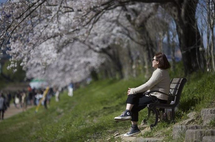 Una mujer se sienta en un banco del parque y mira a lo lejos.