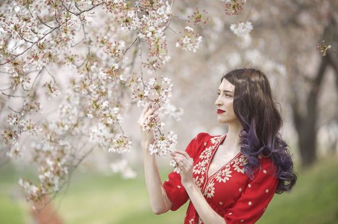 Una modelo femenina con un vestido rojo sosteniendo las ramas de un cerezo en flor