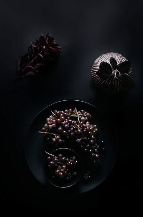 Fotografía cenital de un cuenco de uvas y otros accesorios sobre un fondo oscuro