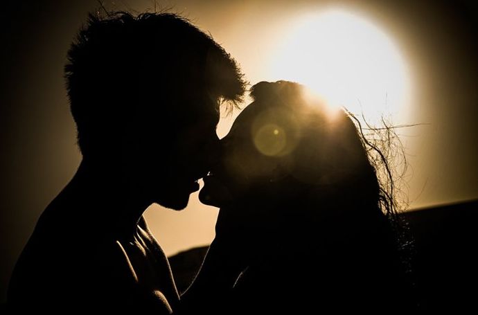 Silueta de una pareja besándose iluminada por el sol como fuente de luz
